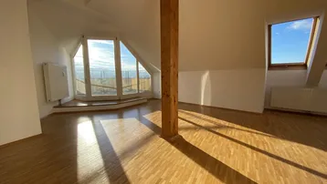 Helles Dachgeschosszimmer mit Holzboden, sichtbarem Holzbalken und Zugang zu einem Außenbereich.