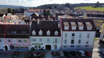 Luftaufnahme einer charmanten Gebäudereihe mit traditioneller Architektur, Geschäften im Erdgeschoss und Blick auf die grüne Landschaft.