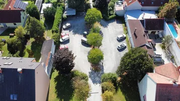 Luftaufnahme eines Parkplatzes umgeben von Wohngebäuden und viel Grünfläche mit einem Pool.