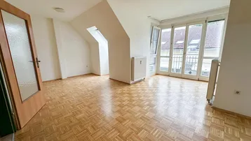 Geräumiges Zimmer im Dachgeschoss mit Parkettboden, Dachschrägen und Zugang zu einem französischen Balkon.