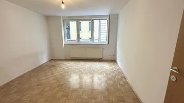 Helles Zimmer mit Fischgrätparkettboden und Blick auf die gegenüberliegende Bebauung.