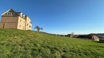 Gebäude auf einem grünen Hügel unter blauem Himmel mit Blick auf die Umgebung.