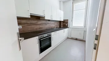 Funktionale Küche mit weißen Schränken, dunkler Arbeitsplatte und Fenster für Tageslicht.