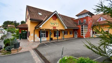 Großes Gebäude mit gelber Fassade, rotem Dach und einem geräumigen Parkplatz davor.