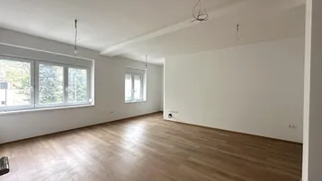 Helles, leeres Wohnzimmer mit Laminatboden und großen Fenstern, bereit zur individuellen Gestaltung.