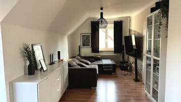 Gemütliches Wohnzimmer mit Dachschrägen, Holzboden und modernem Sofa, ideal zum Entspannen.
