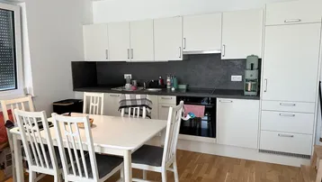 Moderne Einbauküche mit weißen Schränken, dunkler Arbeitsplatte und integriertem Essbereich.
