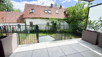 Geräumige Terrasse mit Fliesenboden und Blick auf ein charmantes Altbaugebäude mit Garten.