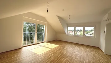 Helles Zimmer mit Holzboden, Dachschrägen und Zugang zu einem französischen Balkon.