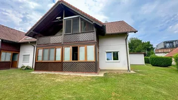 Hausfassade mit großem Gartenbereich und Balkon im Obergeschoss unter bewölktem Himmel.