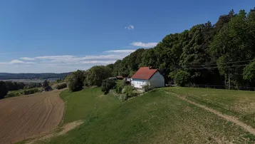 Idyllisches Einfamilienhaus mit rotem Dach auf einem grünen Hügel am Waldrand mit weitem Blick.