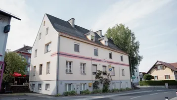 Mehrstöckiges Gebäude mit Satteldach und hellbeiger Fassade an einer Straßenecke.