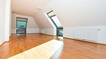 Heller Raum im Dachgeschoss mit Holzboden und großen Dachfenstern, die viel Licht hereinlassen.