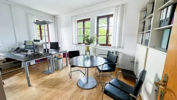 Geräumiges Büro mit Holzboden, zwei Fenstern und modernen Arbeitsplätzen sowie einem Besprechungstisch.