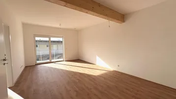 Helles, leeres Zimmer mit Laminatboden, Holzbalken und Zugang zu einem Balkon.