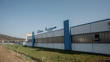 Ansicht des Industriegebäudes mit blauen Akzenten und umliegender Grünfläche unter klarem Himmel.