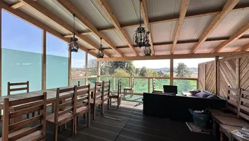 Große überdachte Terrasse mit Holzmöbeln und Sofa, ideal für Entspannung mit weitem Blick ins Grüne.