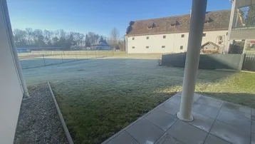 Sonniger Außenbereich mit gepflasterter Terrasse und Blick auf eine weite Rasenfläche.
