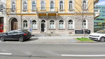 Gelbes Altbaugebäude mit vielen Bogenfenstern und einem kleinen Balkon an der Fassade, von der Straße aus gesehen.