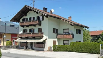 Traditionelles Mehrfamilienhaus mit Holzbalkonen und Blick auf die umliegenden Berge.
