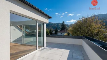 Große Dachterrasse mit hellen Fliesen, Bergblick und Zugang zu einem lichtdurchfluteten Innenraum.