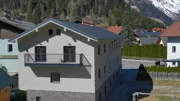 Neubau mit moderner Architektur, Balkon und Steinfassade im alpinen Bergpanorama.