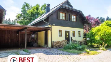 Traditionelles Haus mit Holzverkleidung, gelber Fassade und überdachtem Carport im Grünen.