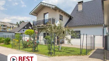 Ansicht des Hauses von außen mit kleinem, eingezäuntem Garten und Balkon im Obergeschoss.