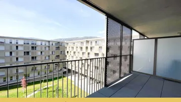 Geräumiger Balkon mit Metallgeländer und Blick auf den begrünten Innenhof der Wohnanlage.