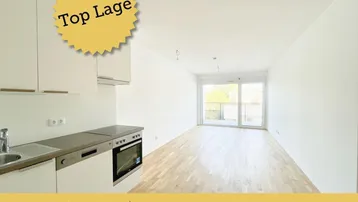 Heller offener Wohnbereich mit integrierter Küchenzeile, Parkettboden und Zugang zu einem Balkon.