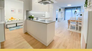 Moderne offene Wohnküche mit hellem Parkettboden und Essbereich, angrenzend an ein Schlafzimmer.