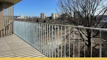 Geräumiger Balkon mit weitem Blick über die Stadt und umliegende Grünflächen unter blauem Himmel.