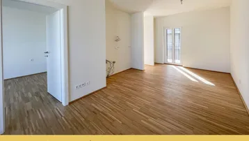 Geräumiger, heller Raum mit Parkettboden und Zugang zu einem französischen Balkon.