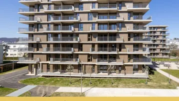 Modernes Mehrfamilienhaus mit vielen Balkonen und Holzfassadenelementen in städtischer Umgebung.