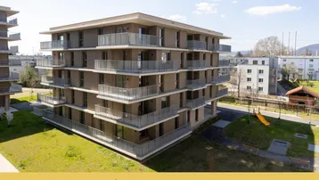 Modernes Mehrfamilienhaus mit mehreren Balkonen und einem kleinen Spielplatz im Außenbereich.