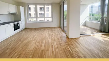 Helles, offenes Wohn-Esszimmer mit integrierter Küche, Parkettboden und Zugang zum Balkon.