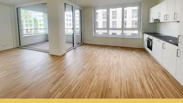 Heller offener Wohn- und Essbereich mit integrierter Küche, Parkettboden und Zugang zum Balkon.
