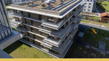 Modernes Wohngebäude mit zahlreichen Balkonen, Gründach und Photovoltaikanlage in grüner Umgebung.
