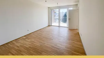 Geräumiger, heller Raum mit Holzparkettboden und großen Fenstern mit französischem Balkon.