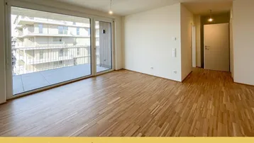 Heller, leerer Wohnbereich mit Parkettboden und großem Schiebefenster zum Balkon.