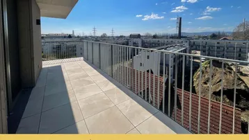Geräumiger Balkon mit Fliesenboden und Blick auf die Umgebung unter blauem Himmel.