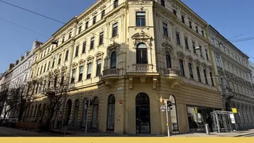 Historisches Eckgebäude mit klassischer Architektur und vielen Fenstern an einer belebten Stadtstraße.