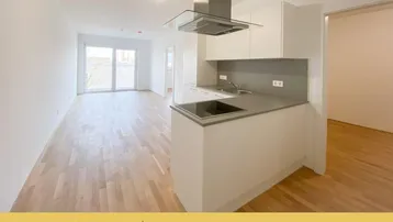 Heller offener Wohnbereich mit moderner Einbauküche, Parkettboden und Zugang zum Balkon.