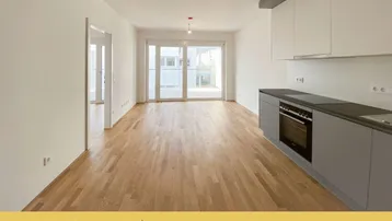 Heller offener Wohnbereich mit integrierter Küche, Parkettboden und Zugang zur Terrasse.
