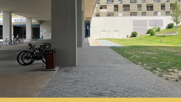 Moderne Gebäudefassade mit gepflastertem Bereich und Grünfläche im Vordergrund.