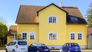 Gelbes Einfamilienhaus mit Satteldach und mehreren Fenstern, davor parken drei Autos.