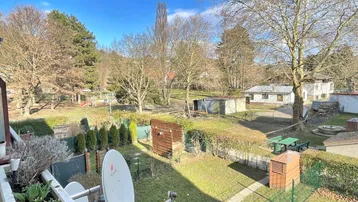 Blick von einem Balkon auf einen gemeinschaftlichen Gartenbereich mit Bäumen, Rasenfläche und einem kleinen Schuppen.