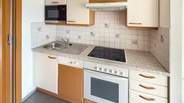 Kompakte Küchenzeile mit integrierten Geräten, Granitarbeitsplatte und Fliesenrückwand.