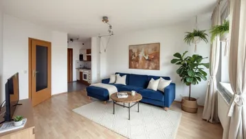 Helles Wohnzimmer mit blauem Sofa, Holzboden und Blick auf die integrierte Küchenzeile.