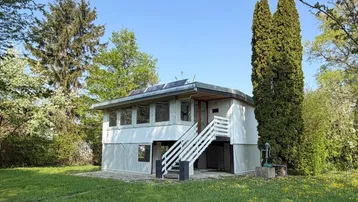Kleines modernes Haus mit Außentreppe und umgebendem Grün in sonniger Lage.